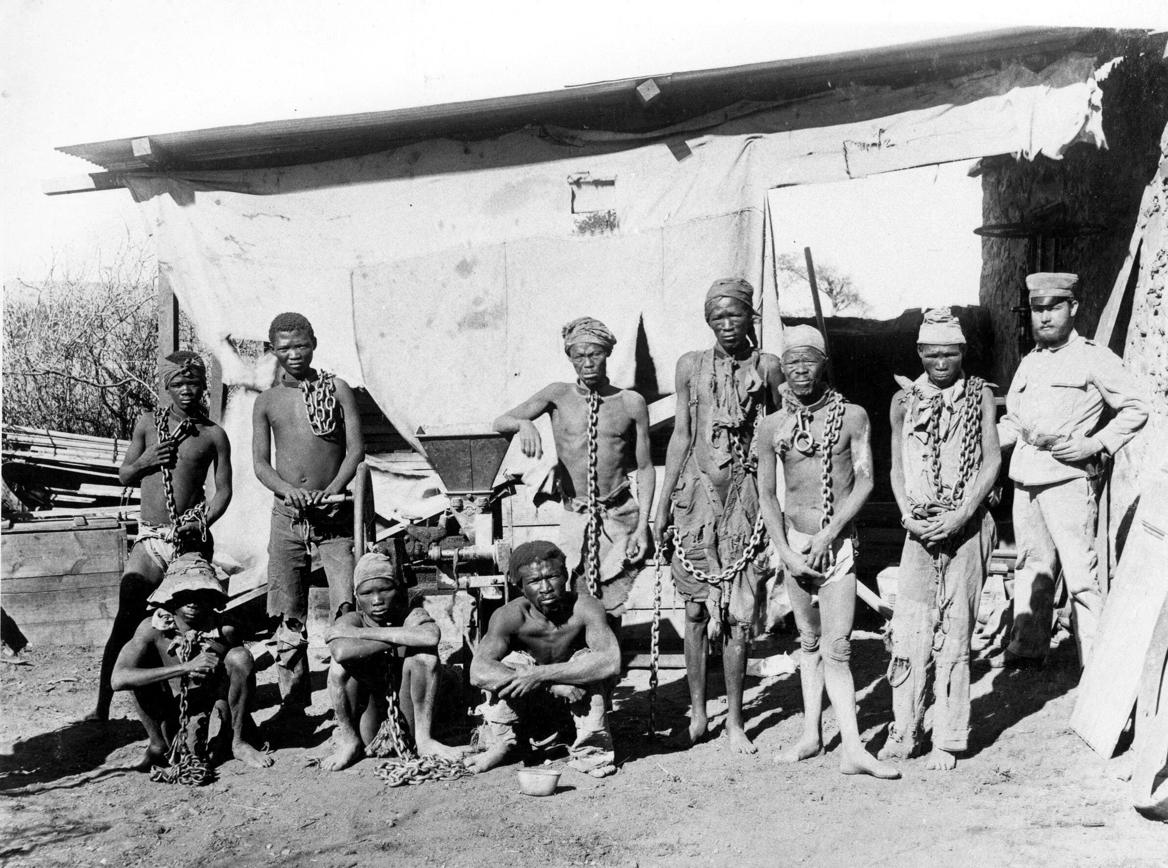 Um grupo de hereros e namas da Namíbia, custodiados por um soldado alemão no começo do século XX.