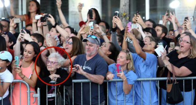 Idosa observa atores enquanto público tenta fotografá-los.