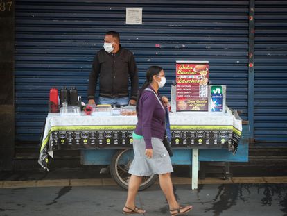 Uma mulher passa por um vendedor ambulante no centro de São Paulo, ambos usando máscara de proteção, nesta segunda-feira.