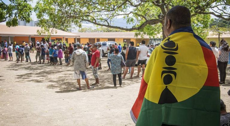 Homem com a bandeira da Nova Caledônia aguarda para votar.