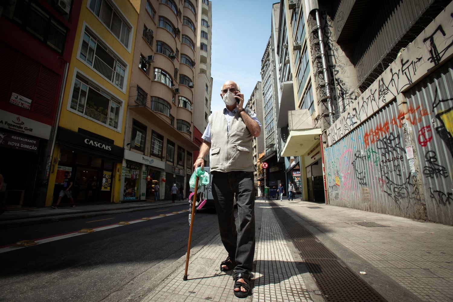 O padre Julio Lancellotti caminha pelas ruas do centro de São Paulo enquanto fala no telefone celular.