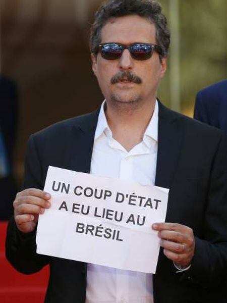 No tapete vermelho de Cannes, Kleber Mendonça Filho segura cartaz no qual denuncia que “um golpe de Estado aconteceu no Brasil”.