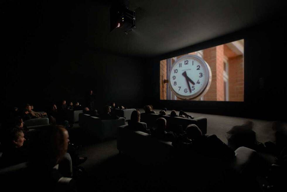 Pessoas assistindo ao filme 'The Clock' de Christian Marclay.
