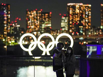 Casal faz selfie diante dos anéis olímpicos em Tóquio.