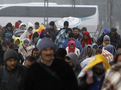 Imigrantes e refugiados cruzam fronteira sob chuva.