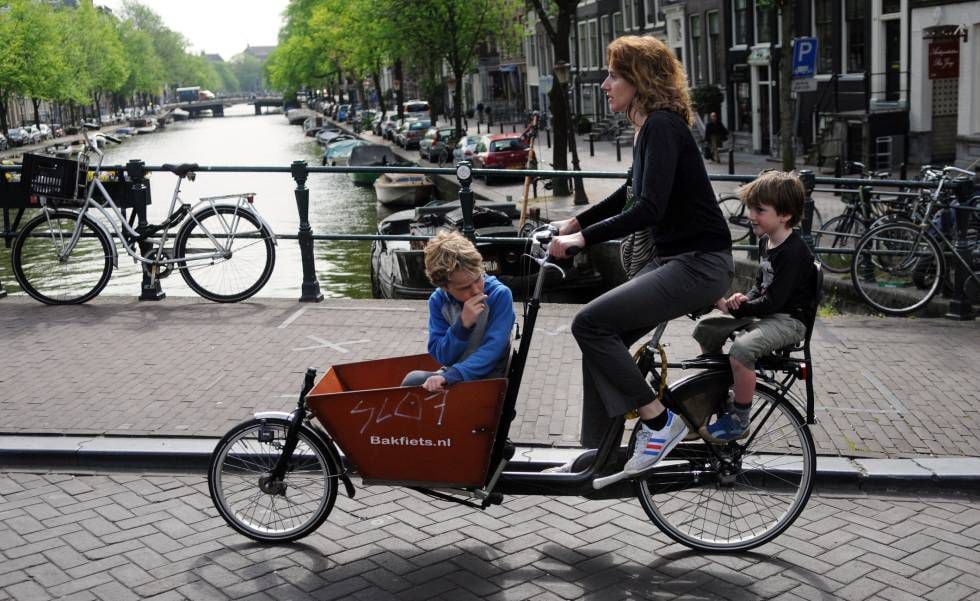 Mãe com os filhos atravessando de bicicleta um dos canais de Amsterdã.