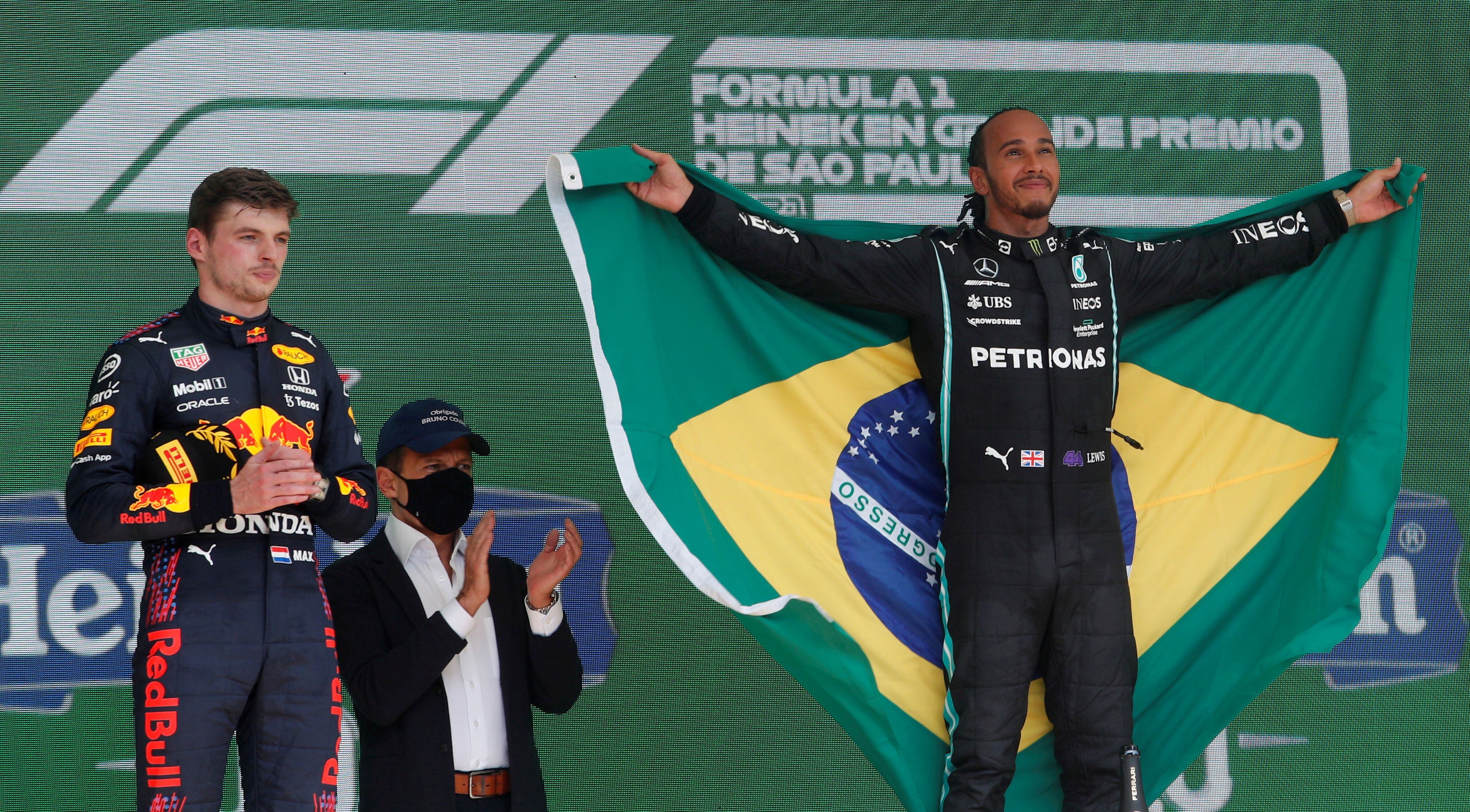 Verstappen, em segundo, e Hamilton, em primeiro com a bandeira do Brasil.