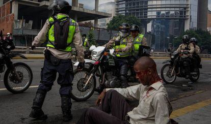 Homem ferido junto a policiais da Guarda Nacional Bolivariana.