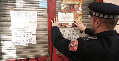 Policial municipal coloca um cartaz numa loja fechada por vender bebida alcoólica a menores em Madri.