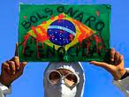 A demonstrator holds an image of the Brazilian flag covered in fake blood and the Portuguese phrase "Bolsonaro Genocide" during an anti-government protest by unions against President Jair Bolsonaro's policies to fight the COVID-19 pandemic in Brasilia, Brazil, Wednesday, May 26, 2021. (AP Photo/Eraldo Peres)