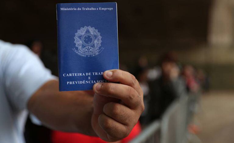 Um homem exibe sua carteira de trabalho enquanto aguarda na fila por emprego em São Paulo: idade mínima para aposentadoria deve ficar em 65 anos para homens e 62 para mulheres.