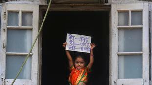 Menina indiana segura cartaz onde se lê "Ninguém deve sair de casa", em Mumbai.