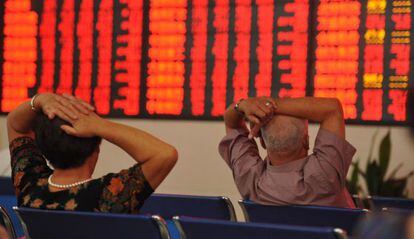 Dois investidores observam um painel com cotações da Bolsa na China.