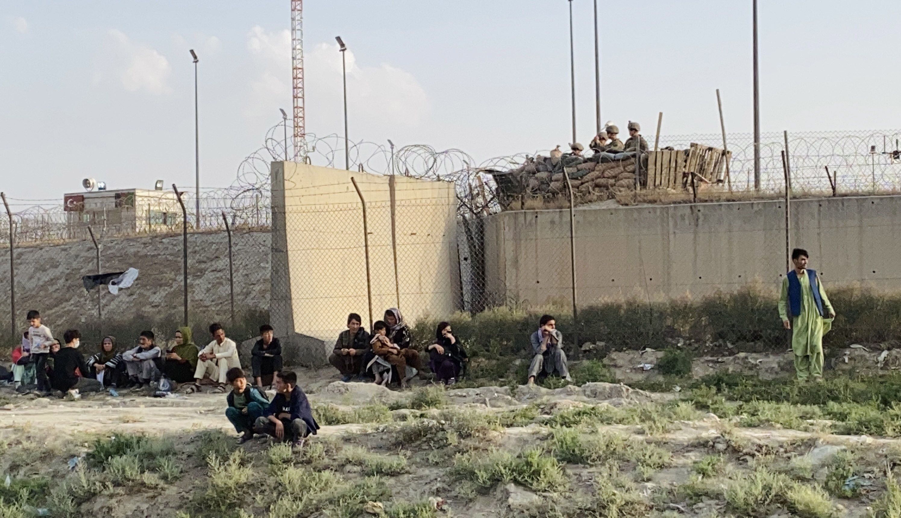 Um grupo de pessoas aguarda nos acessos do aeroporto de Cabul.  