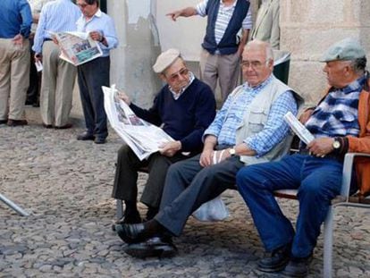 Aposentados portugueses leem jornais em uma rua.