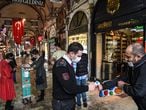 A security officer checks a visitor's body temperature, as two women behid clean their hands with disinfectant gel as people enter the iconic Grand Bazaar after reopening restaurants, cafes in Istanbul on June 1, 2020. - Turkey reopened restaurants, cafes and Istanbul's iconic 15th century Grand Bazaar market on June 1, as the government further eased coronavirus restrictions. Many other facilities including parks, beaches, libraries and museums also reopened across the country, while millions of public sector employees returned to work. (Photo by Ozan KOSE / AFP)