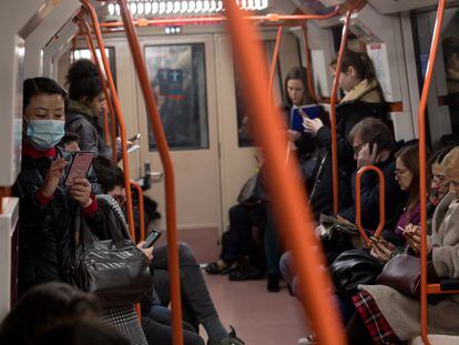 Mulheres no metrô de Madri usando máscaras enquanto olham para o celular.