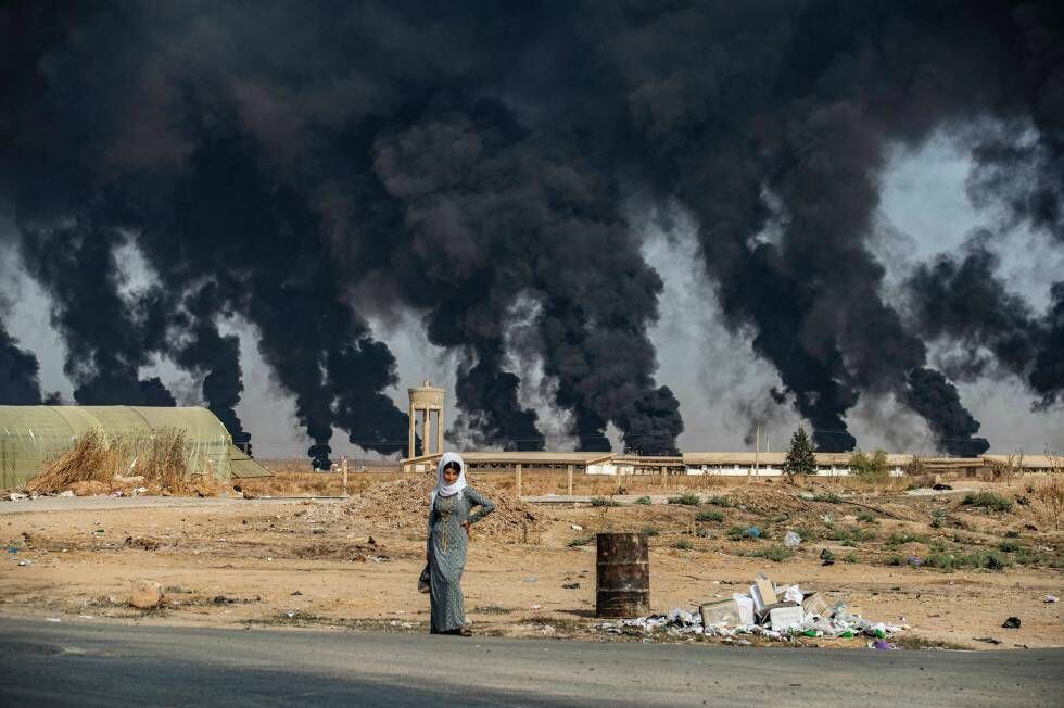 Uma mulher na frente da fumaça de pneus queimados pelos curdos para dificultar a visibilidade da aviação turca.