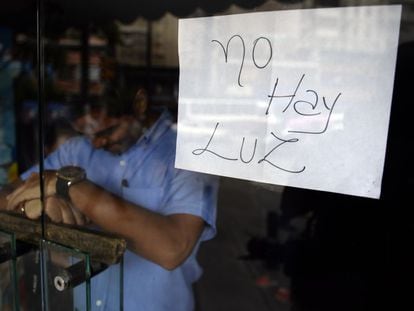 Empregado atrás da porta de uma loja fechada em Caracas, onde um cartaz avisa: “Não há luz”.