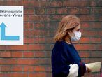 A woman, wearing a face mask, walks past a sign guiding people to the entrance of a corona testing station at the Vivantes Wenckebach hospital in Berlin on March 13, 2020. - German Chancellor Angela Merkel called on organisers of non essential events gathering hundreds of people to cancel them to help slow the spread of coronavirus. The regional governments of Germany's 16 states will decide if they want to shutter school gates according to the local situation, Merkel said on March 13, 2020, adding that an option could be to bring forward April's Easter school holidays. (Photo by Odd ANDERSEN / AFP)
