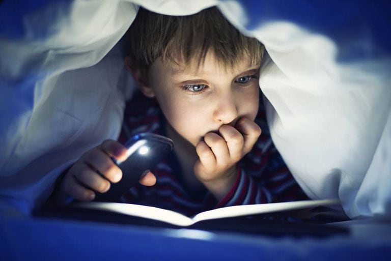 Menino lendo um livro iluminado pela luz do celular