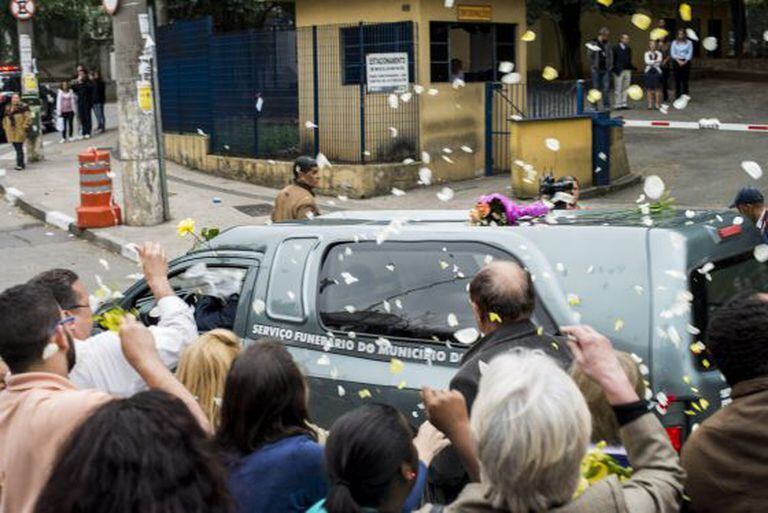 Pessoas jogam pétalas sobre o carro com os restos mortais das vítimas.