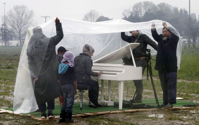 O artista Ai Weiwei (à direita) assiste à apresentação de piano da síria Nour Al Khizam no campo de refugiados situado na fronteira da Grécia com a Macedônia em 12 de março.
