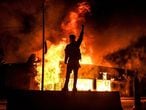 TOPSHOT - A protester reacts standing in front of a burning building set on fire during a demonstration in Minneapolis, Minnesota, on May 29, 2020, over the death of George Floyd, a black man who died after a white policeman kneeled on his neck for several minutes. - Violent protests erupted across the United States late on May 29 over the death of a handcuffed black man in police custody, with murder charges laid against the arresting Minneapolis officer failing to quell seething anger. (Photo by Chandan KHANNA / AFP)