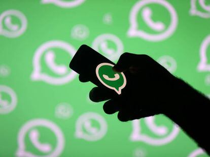 Um homem com um móvel posa em frente a uma tela com o logotipo de WhatsApp.