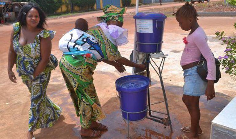 Três mulheres lavam as mãos na entrada do hospital de Kipe, na Guiné.