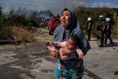 Uma refugiada foge do fogo com seu bebê nos braços.
