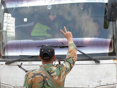 Soldados sírios fazem o símbolo da vitória em frente a um ônibus que evacua rebeldes em Duma, nos arredores de Damasco.