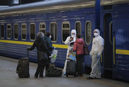 Trabalhadores com macacão de proteção verificam os documentos dos passageiros prestes a embarcar, na estação de Kiev, em um trem para Moscou.