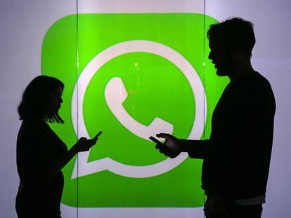 Duas pessoas usam seus celulares em frente ao logo do WhatsApp em Londres.