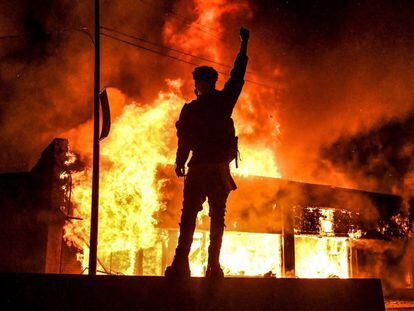 Un manifestante alza un brazo frente a un edificio en llamas incendiado durante una manifestación en Minneapolis.