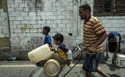 Pai e filhos carregam galões de água em Caracas