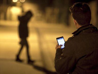 Um homem usa seu celular diante da silhueta de uma jovem.