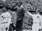 Jesse Owens en el podio olímpico después de su victoria en el salto de longitud en los Juegos Olímpicos de Berlín 1936 junto a Naoto Tajima (izquierda) y Luz Long (derecha). El la entrega de la cuarta medalla de oro a Owens, Hitler se limitó a abandonar el estadio para no verse obligado a estrechar la mano del atleta negro. 