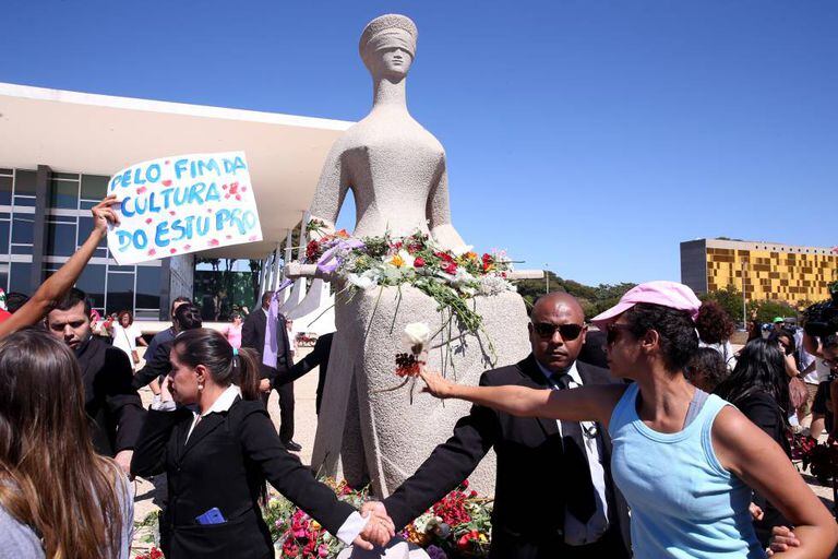 Mulheres protestam depositando flores na estátua da Justiça, em Brasília