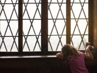 Uma menina espera junto a uma janela.