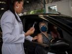 A Public Health worker gives a flu vaccine to a woman at a drive-through model in Tijuca neighbourhood in Rio de Janeiro, Brazil, on March 24, 2020. - The Rio de Janeiro state government is requesting people not to go to the beach or any other public areas as a measure to contain the coronavirus pandemic. (Photo by Mauro PIMENTEL / AFP)