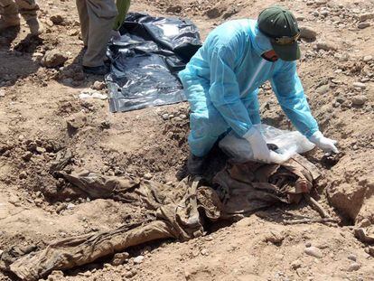 Um membro das forças de segurança iraquianas examina os restos de uma pessoa em uma vala comum em Tikrit, em abril de 2015.