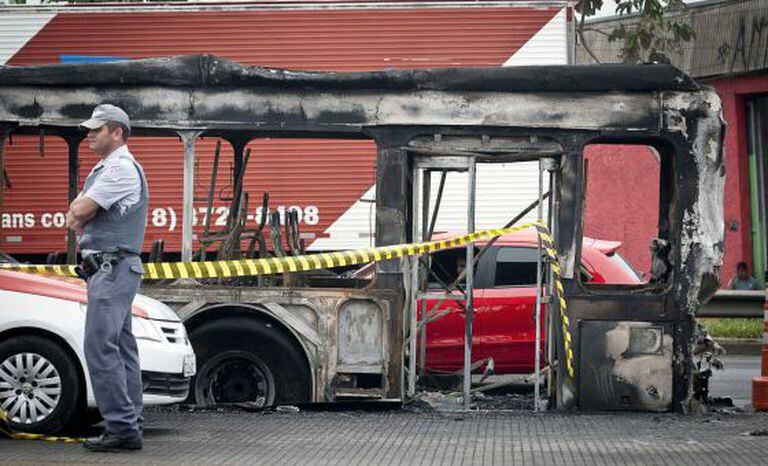 Um policial em frente a um ônibus queimado na zona sul de São Paulo.