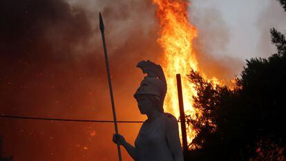 Uma estátua da deusa grega Atena, iluminada por um incêndio ao fundo, em Varympompi, norte de Atenas, na Grécia, em 3 de agosto.