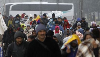 Imigrantes e refugiados cruzam fronteira sob chuva.