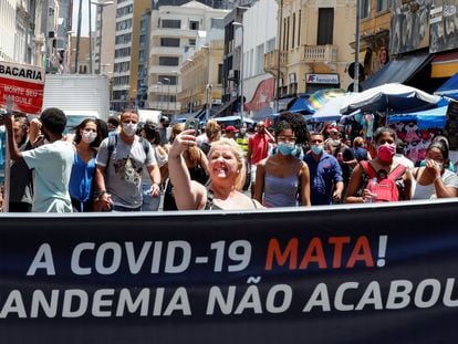 Uma mulher sem máscara tira uma 'selfie' atrás de uma faixa no centro de São Paulo que, em 18 de dezembro, lembrava que a pandemia não acabou no Brasil.