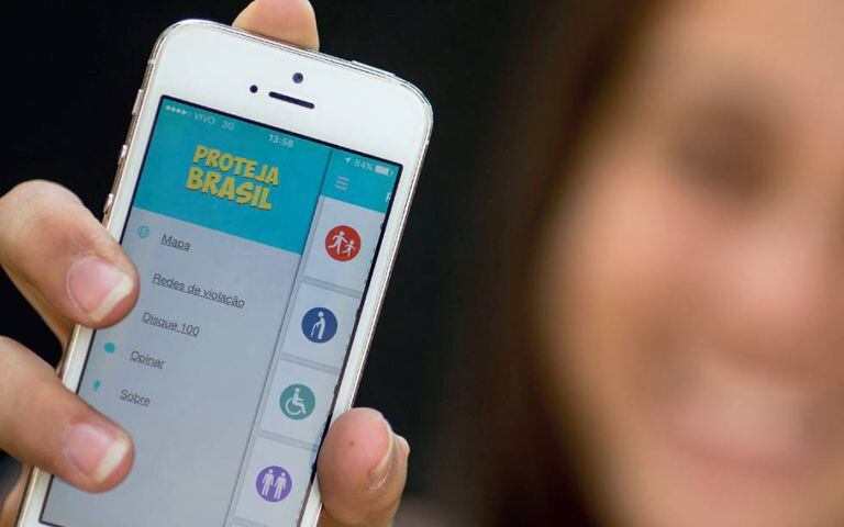 Jovem segura celular com o 'app' do Proteja Brasil.