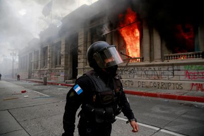 Policial caminha ao lado do Congresso em chamas na Cidade da Guatemala, neste sábado.