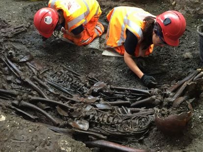 Dois arqueólogos escavam uma vala comum com vítimas da peste em Londres.