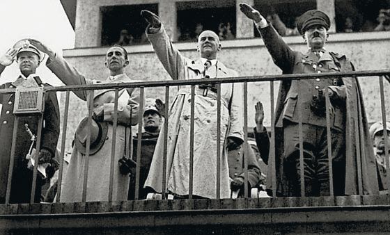 Adolf Hitler realiza a saudação nazista junto a outros membros do partido nas grades do campo de regatas de Grünau.